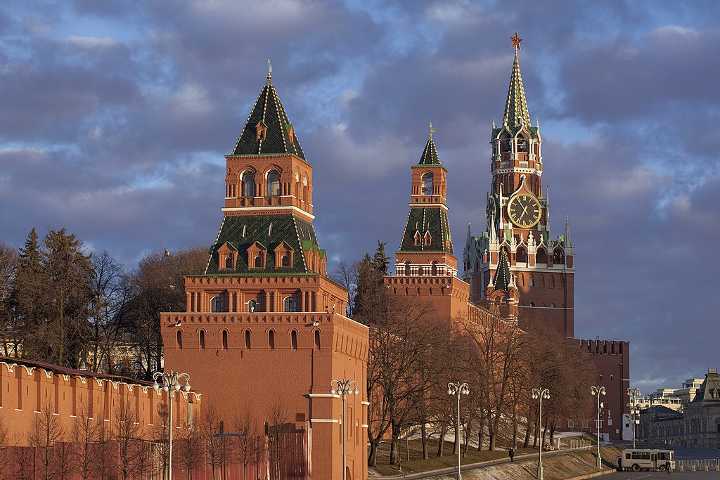 Rødbrun mur med tre tårn, hvorav det største har en stor klokke og en rød stjerne på spiret. Foto