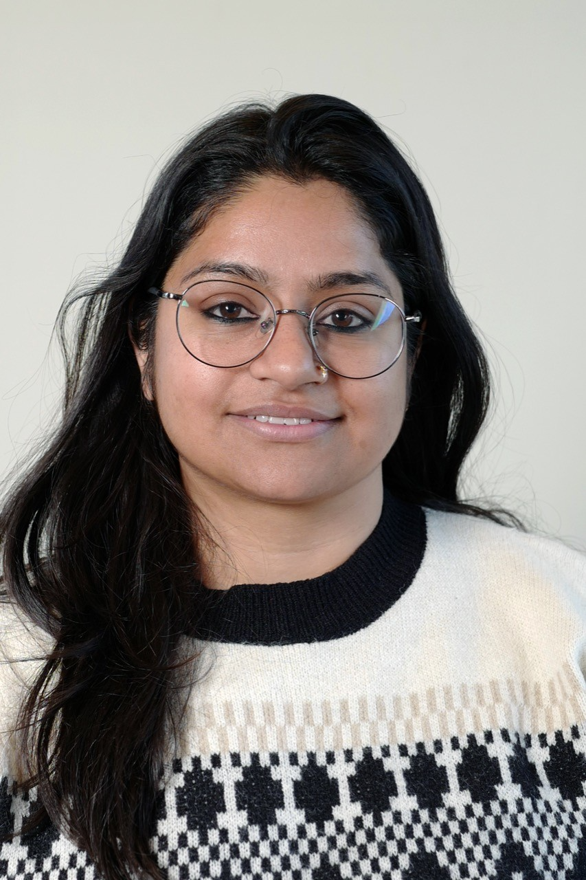 Event Officer Reetika smiling in front of the camera wearing glasses and a wool jumper in front of a white background