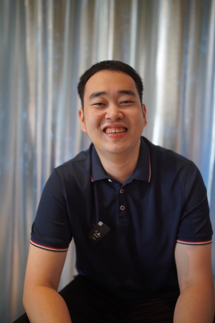PR Officer Tianfang is smiling cheerfully in front of a sliver curtain background