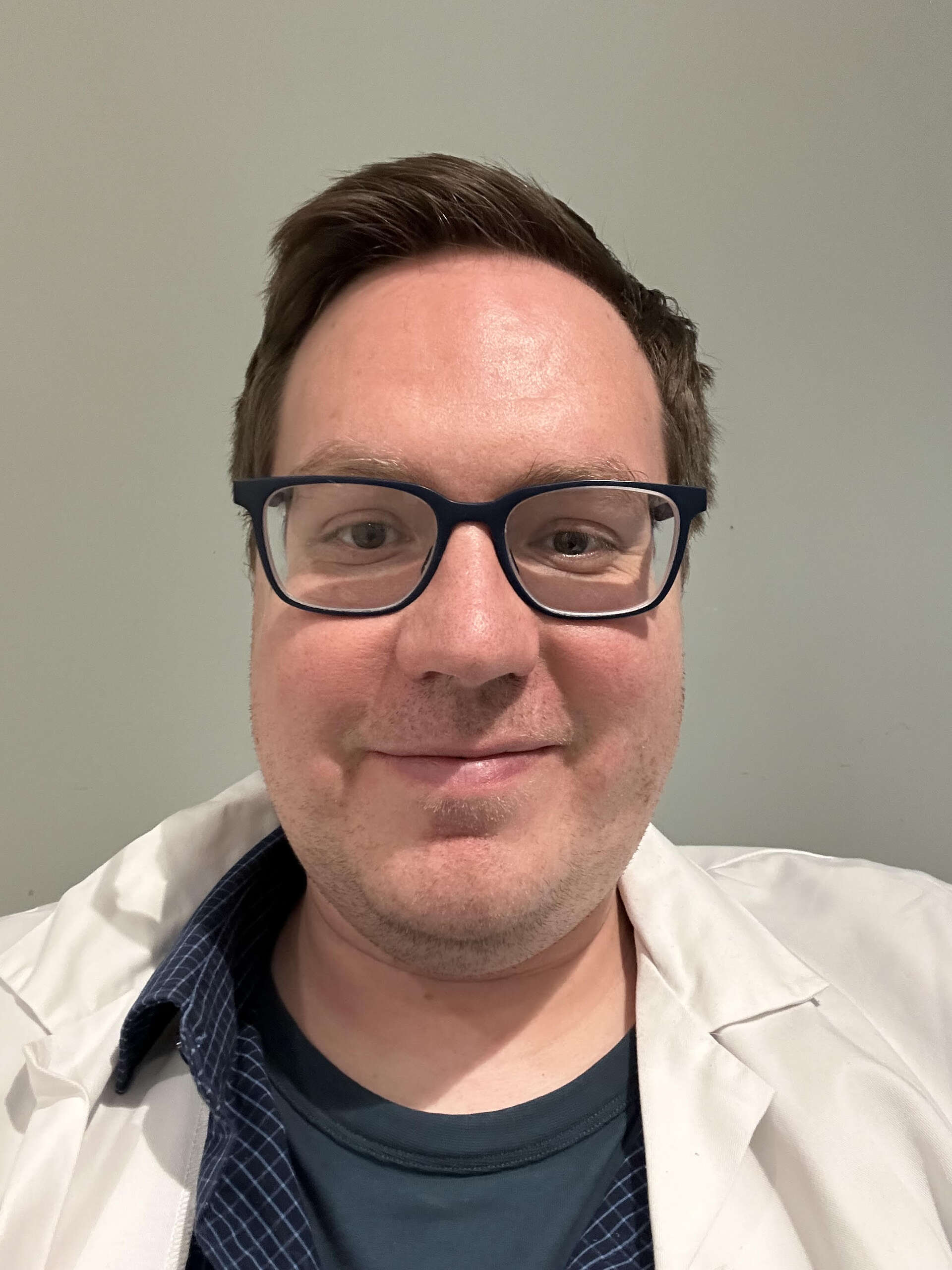 PR Officer Karl Henrik smiling with glasses wearing a doctor coat in front of a beige background.