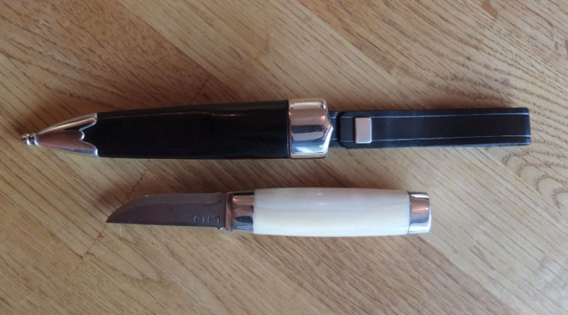 Kniv av Torgeir Brun Johnsen
Total lengde 20,5 cm.
Knivblad 5,1 cm.
Skaft 7,8 cm.
Slire av masurlær og sølv.
Skaft av hvaltann og sølv